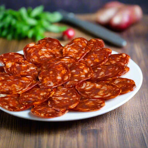 Large plate of sliced chorizo with some onions, greens and a knife blurred in the background