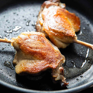 Two cooked duck legs on a black plate