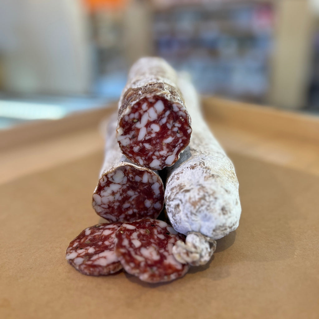 multiple sticks of salami stacked on top of each other, two with the faces cut and couple thick slices in the foreground