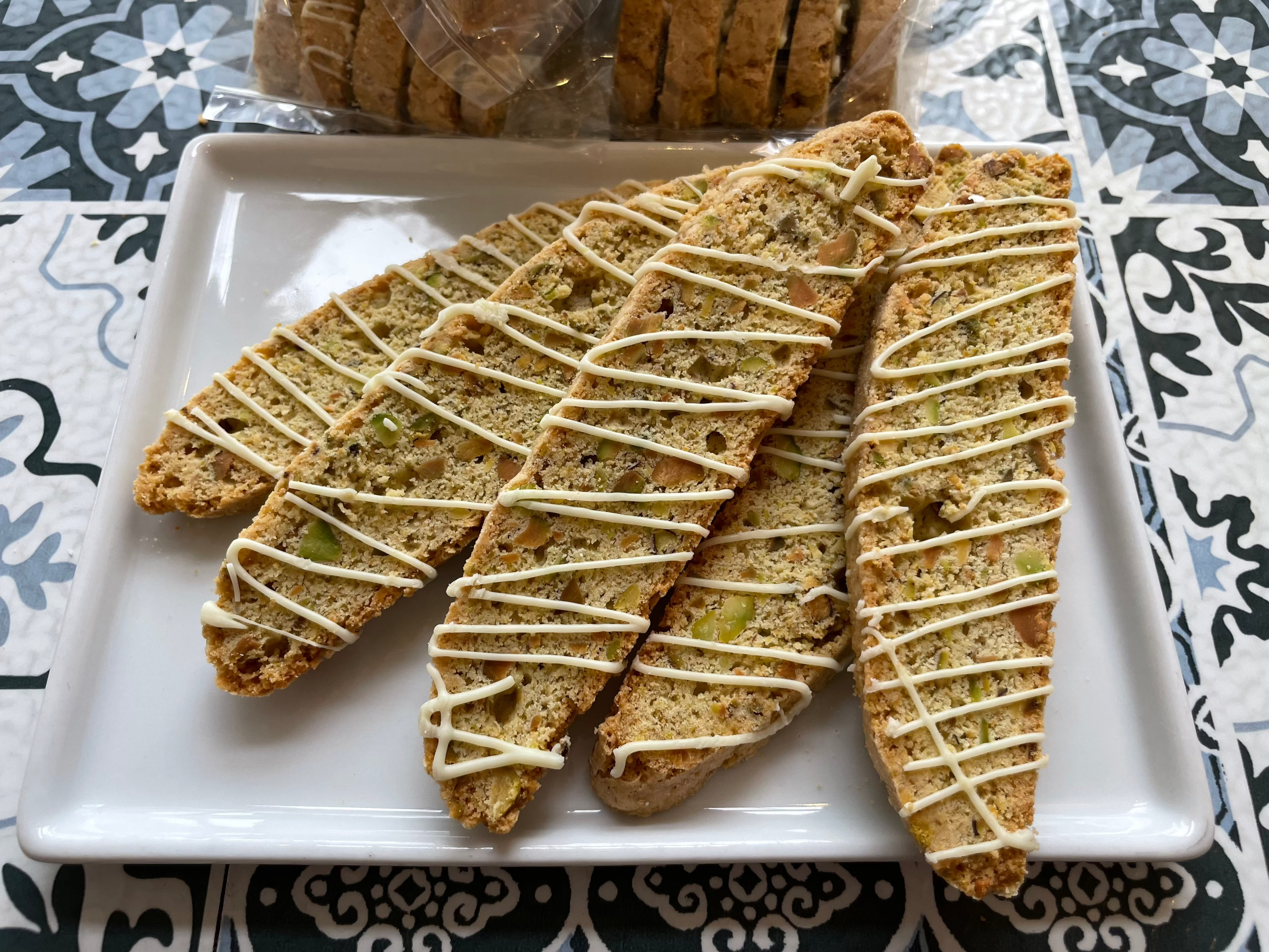 close-up shot of biscotti lemon pistachio, on a square white plate, with chunks of pistachio in bread, with slight white chocolate zig zag drizzle