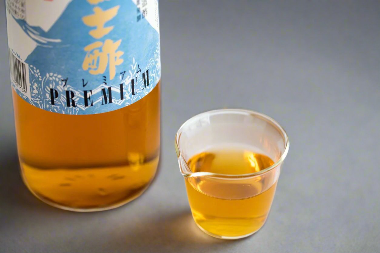 Glass bottle of rice wine vinegar, alongside a small glass cup of vinegar