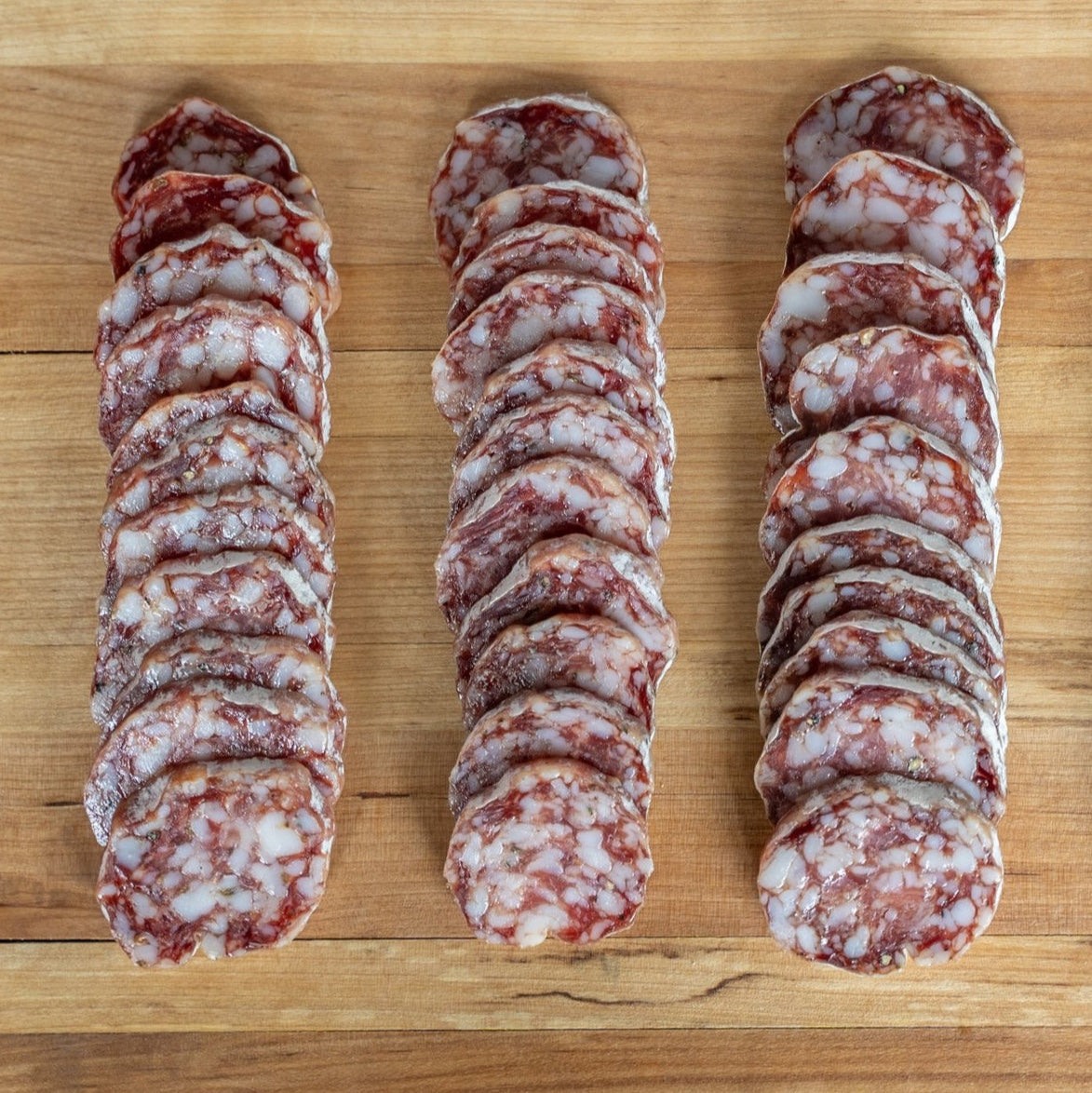 3 rows of thickly sliced salami on a wood board, 9 slices per row.