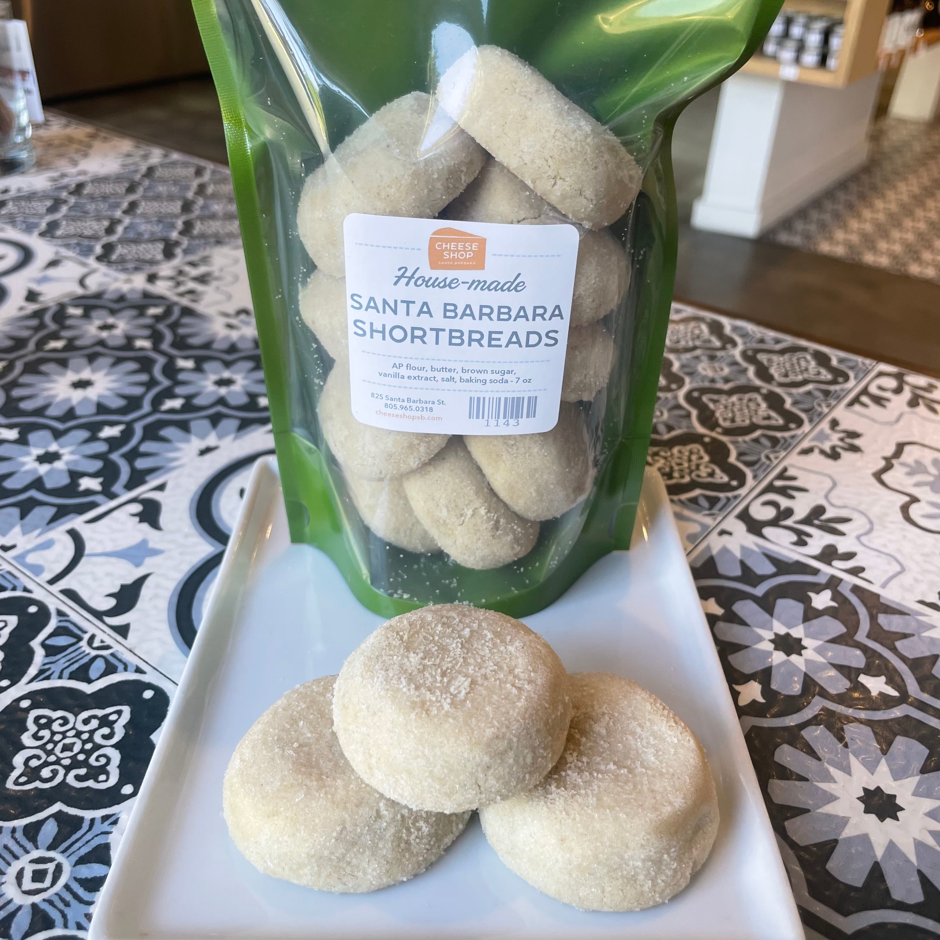 green bag of housemade half-round santa barbara shortbread cookies, with 3 cookies on a white plate, visible granular sugar ontop