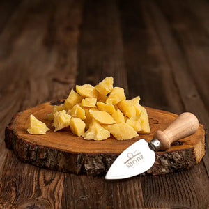 Cubed and cut up sbrinz cheese, a yellow hard cheese, ontop of a wooden board on a wood table, next to a cheese knife