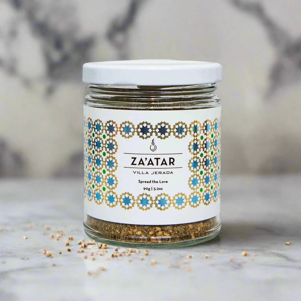small glass jar of za'atar spices, with spices on the table