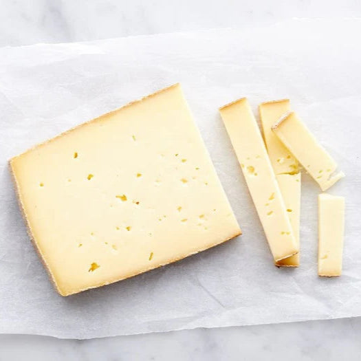 small wedge of yellow paste cheese, with a few slices next to it, small holes in cheese