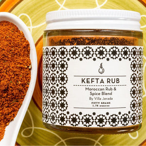 Glass jar of kefta rub, with orange/red seasoning in a white spoon